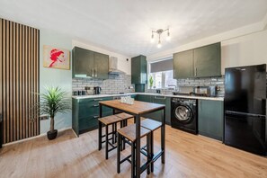 Eine moderne Küche mit dunkelgrünen Schränken, einem Holztisch und einer Waschmaschine.