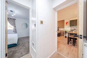 Ein Hotelzimmer mit einem Bett, einem runden Spiegel, einem Fenster mit Vorhängen und Blick auf einen Küchenbereich mit Holztisch und Stühlen.
