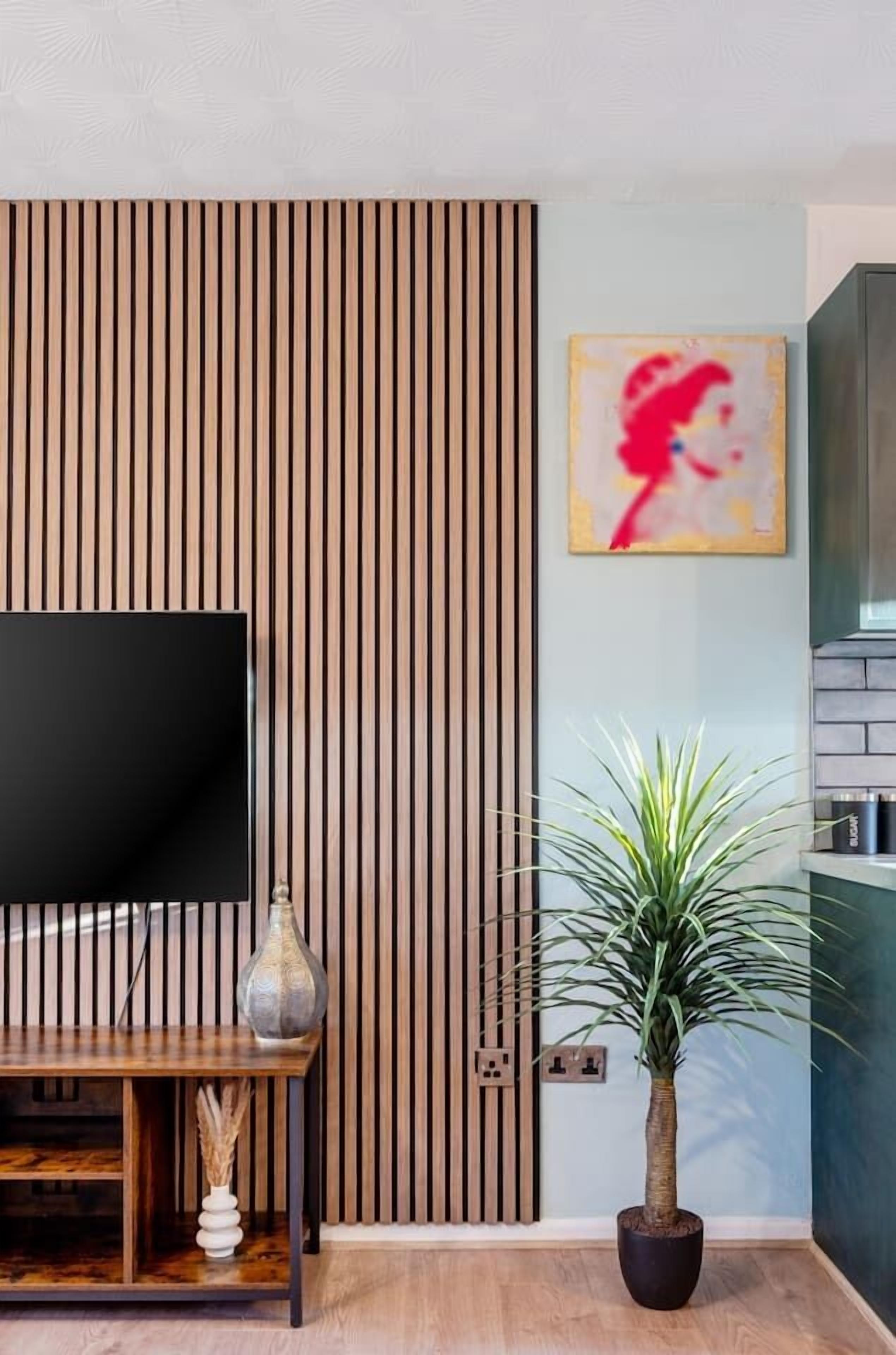 A modern living room with a flat-screen TV, a wooden slat wall, a potted plant, and a painting.