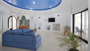 Ein großzügiges Wohnzimmer mit einem blauen Sofa, einem an der Wand montierten Fernseher und einer Decke mit blauem Muster.