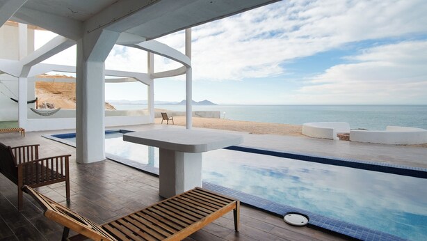 Ein Poolbereich mit Meerblick, Holzmöbel und einer Hängematte.
