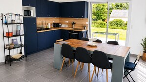 Une cuisine moderne avec des meubles de couleur bleu foncé, une table à manger en bois et une vue sur le jardin.