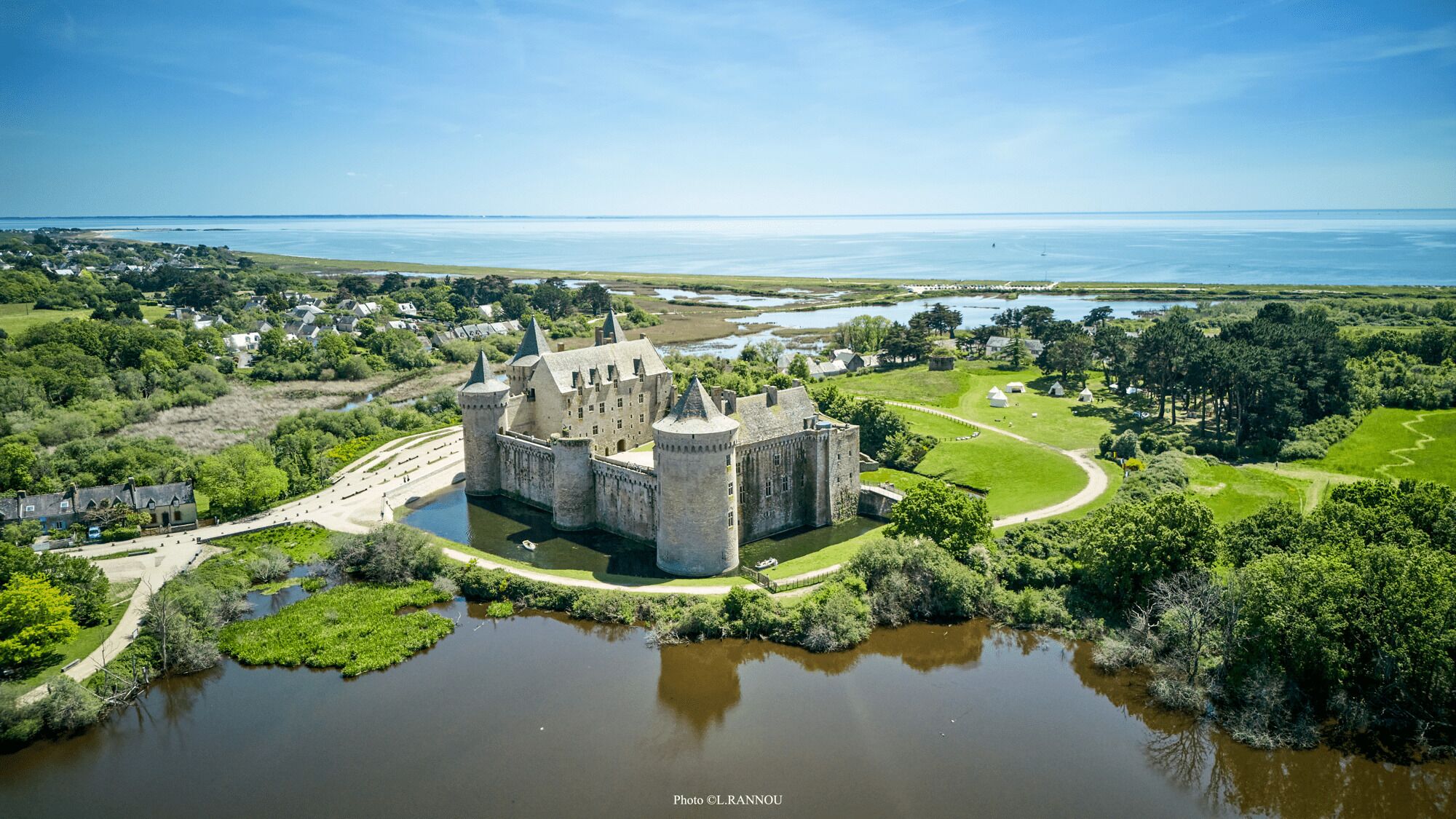 A castle surrounded by water, greenery, and a clear sky.