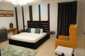 Une chambre moderne avec un lit noir, du linge de lit blanc, un tapis moelleux, un fauteuil jaune et un tableau accroché au mur.