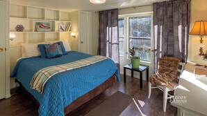 Un dormitorio acogedor con una cama grande, una mesita de noche con lámpara, una silla y una ventana con cortinas.