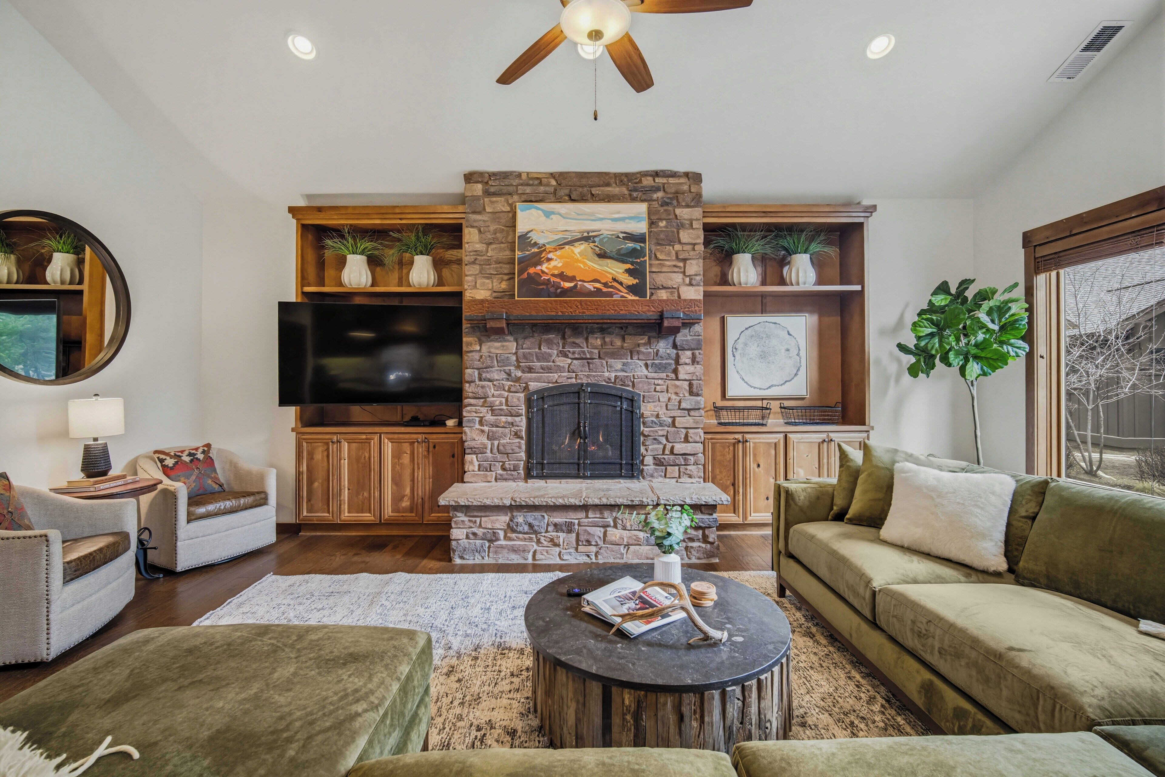 A living room with a stone fireplace, a television, and a ceiling fan.