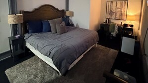 Een slaapkamer met een bed, twee nachtkastjes, een bureau, een stoel, een lamp en een schilderij aan de muur.