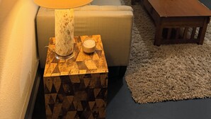 Een gezellige woonkamer met een lamp op een bijzettafeltje met dessin, een bank, een houten salontafel met een bloemenvaas, en een stoel.