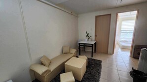 A living room with a sofa, a small table with a plant, and a door leading to a balcony. - URBAN DECA ORTIGAS SM EAST PASIG (Pasig)