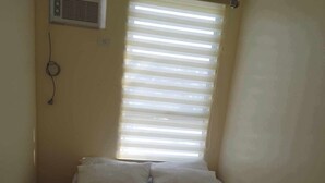 A small, single-bed room with a window and an air conditioning unit. - URBAN DECA ORTIGAS SM EAST PASIG (Pasig)