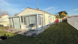 Ein Haus mit umzäuntem Garten, einer Terrasse mit Tisch und Stühlen und einem strahlend blauen Himmel.