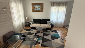 Ein Wohnzimmer mit einer Couch, einem Glastisch und einem gemusterten Teppich.