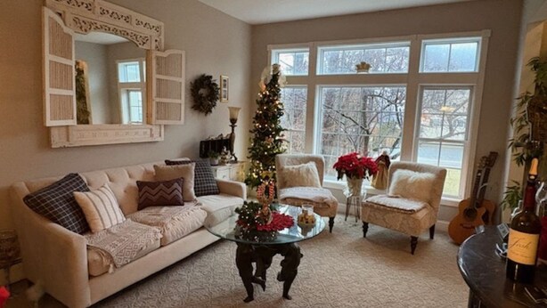 Ein gemütliches Wohnzimmer mit einem beige farbenen Sofa, einem Glastisch und einem Weihnachtsbaum. Zwei Sessel und ein Kamin sind ebenfalls vorhanden.