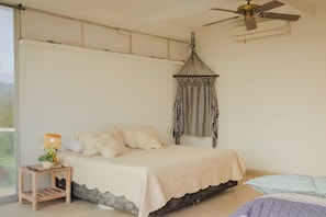 Un dormitorio con cama, una mesita de noche con lámpara, una lámpara colgante y un ventilador de techo.