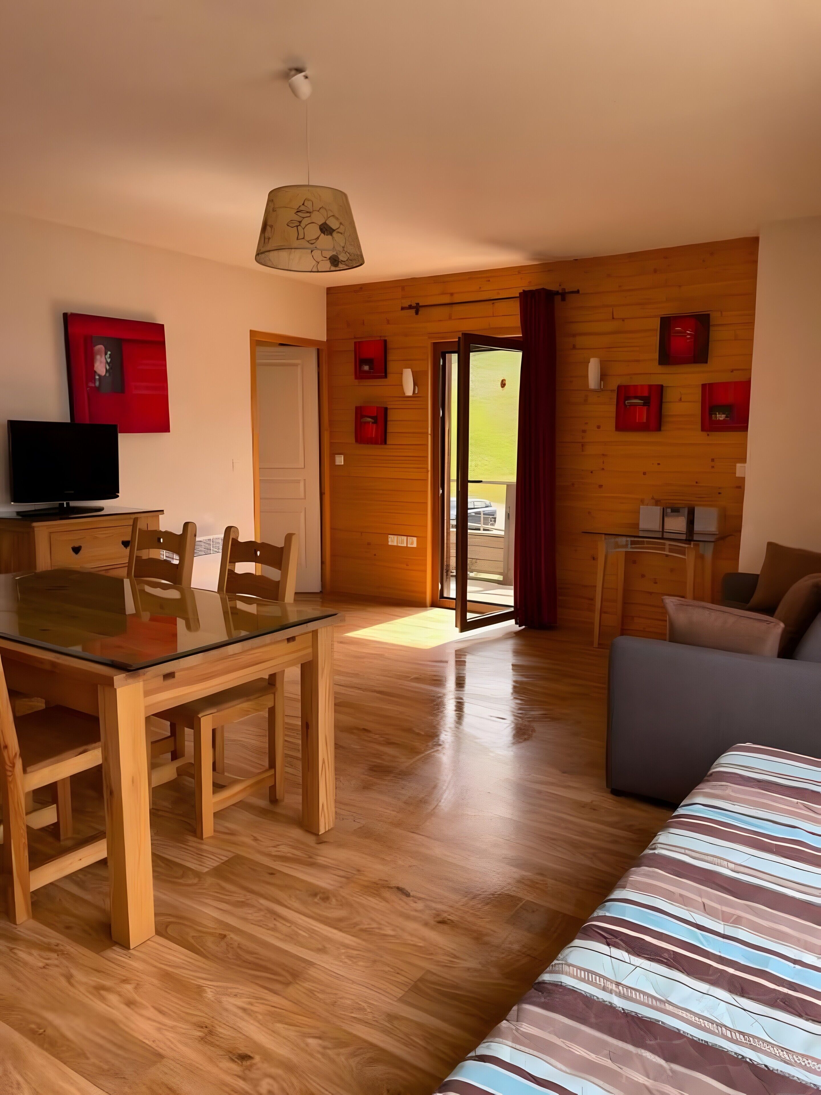 Una habitación con suelo de madera, una mesa de comedor con sillas, un sofá, un televisor y una puerta que da al exterior.
