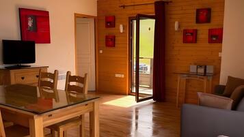 Una habitación con suelo de madera, una mesa de comedor con sillas, un sofá, un televisor y una puerta que da al exterior.
