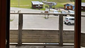 A view from a window overlooking a parking area with a grassy hill, a small building, and a clear sky.