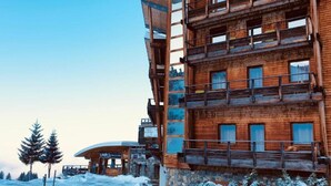A multi-story wooden building with balconies, a sign indicating a spa, and snow-covered surroundings.