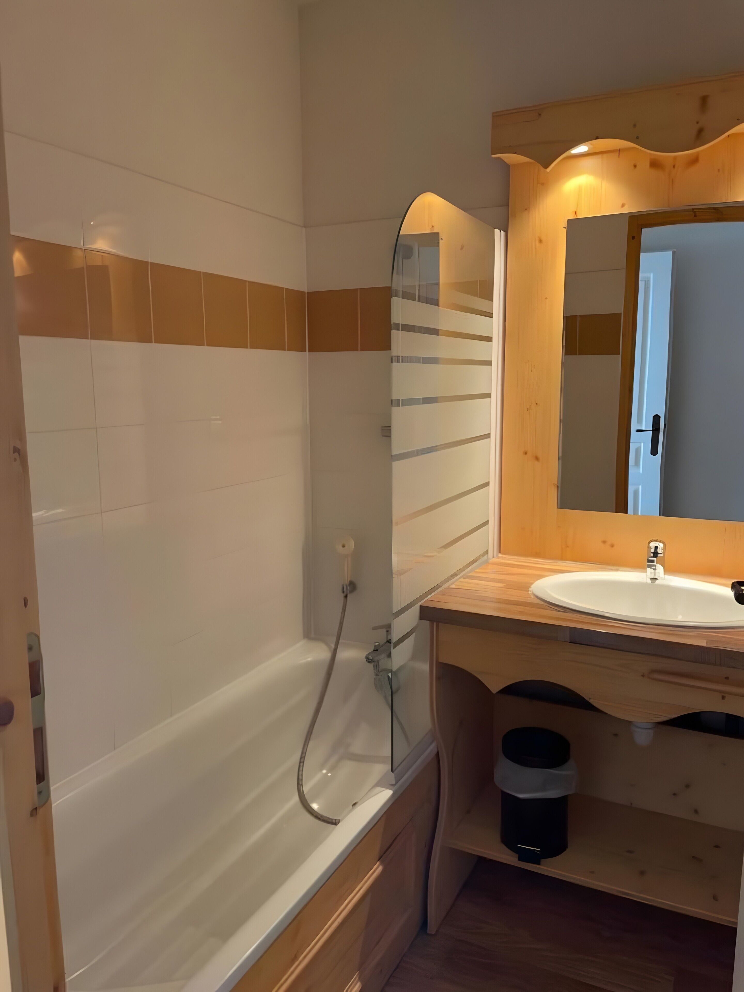 Une salle de bain avec une baignoire, un meuble-lavabo en bois avec un évier, un miroir et un espace douche.