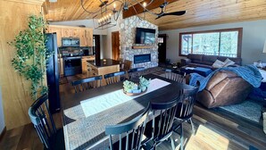 A modern kitchen with wooden cabinets, a stone fireplace, and a dining area with a large table and chairs.