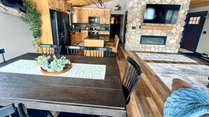 A modern kitchen with wooden cabinets, a stone fireplace, and a dining area with a dark wooden table and chairs.