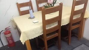 Un comedor con una mesa dispuesta para dos personas, sillas de madera, un jarrón con flores y un extintor.
