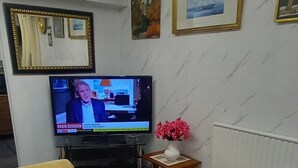 A living room with a sofa, a television, a framed picture, and a vase with flowers.