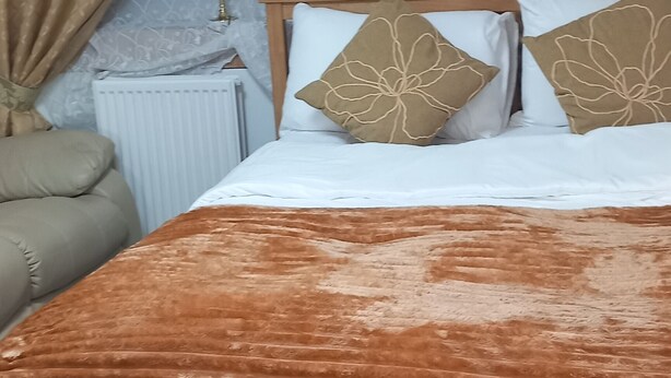 A bedroom with a wooden bed, beige curtains, a white radiator, and a checkered floor.