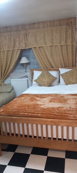 A bedroom with a wooden bed, beige curtains, a white radiator, and a checkered floor. - Two bedroom apartment with all facilities. 6 min walk to the beach (Skegness)