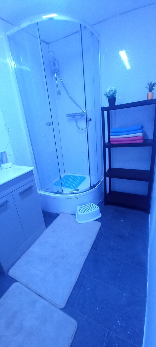 A bathroom with a glass shower enclosure, a sink, a toilet, and a shelf with folded towels.