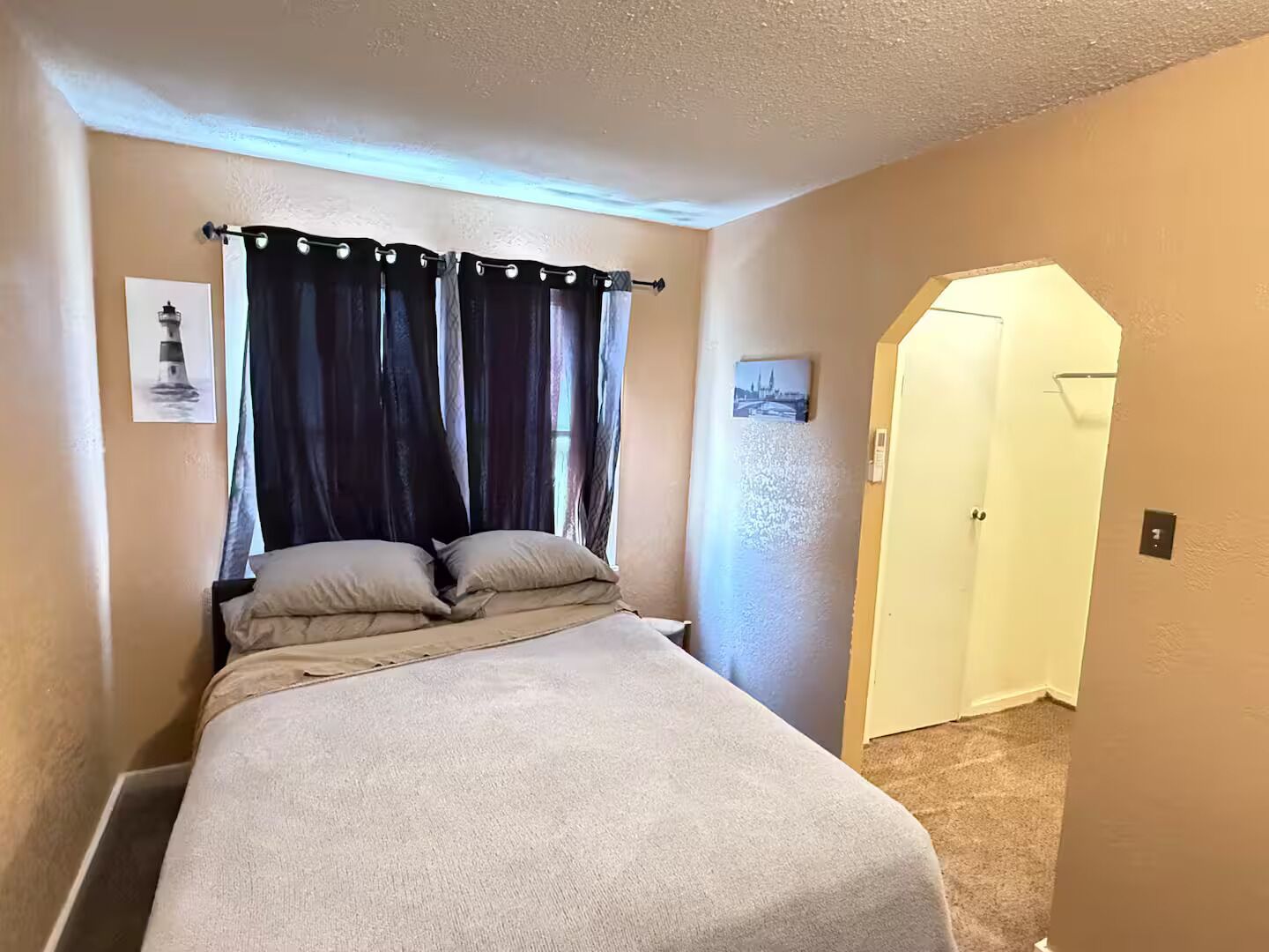 A bedroom with a bed, curtains, a door, and two wall-mounted pictures.