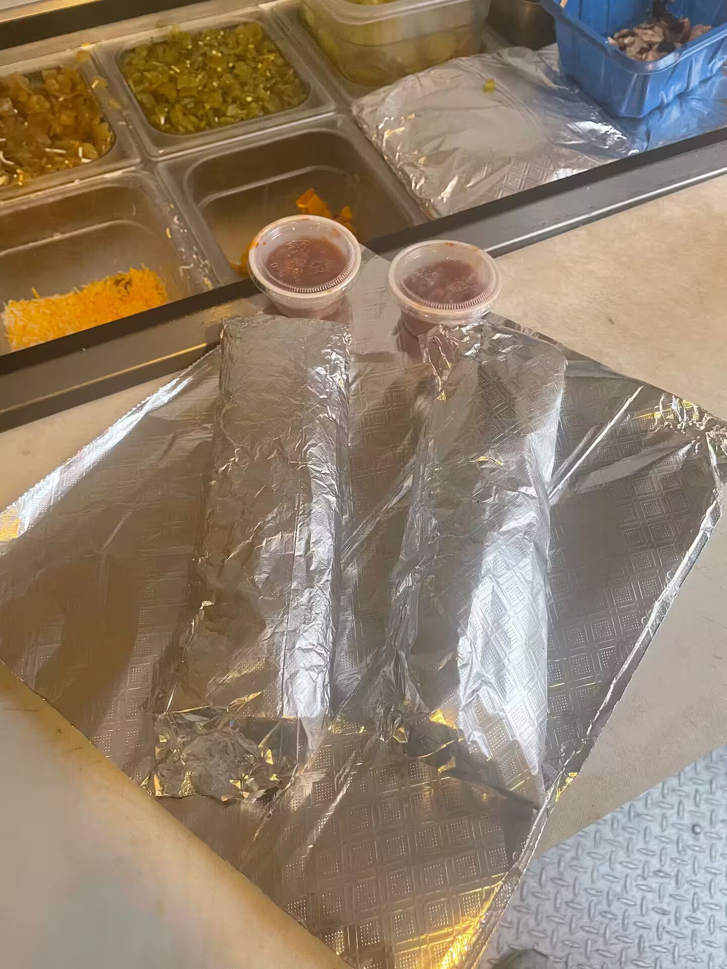 Une présentation de produits alimentaires comprenant divers récipients contenant différents aliments et deux petites tasses posées sur une surface recouverte de papier d’aluminium.
