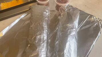 Une présentation de produits alimentaires comprenant divers récipients contenant différents aliments et deux petites tasses posées sur une surface recouverte de papier d’aluminium.