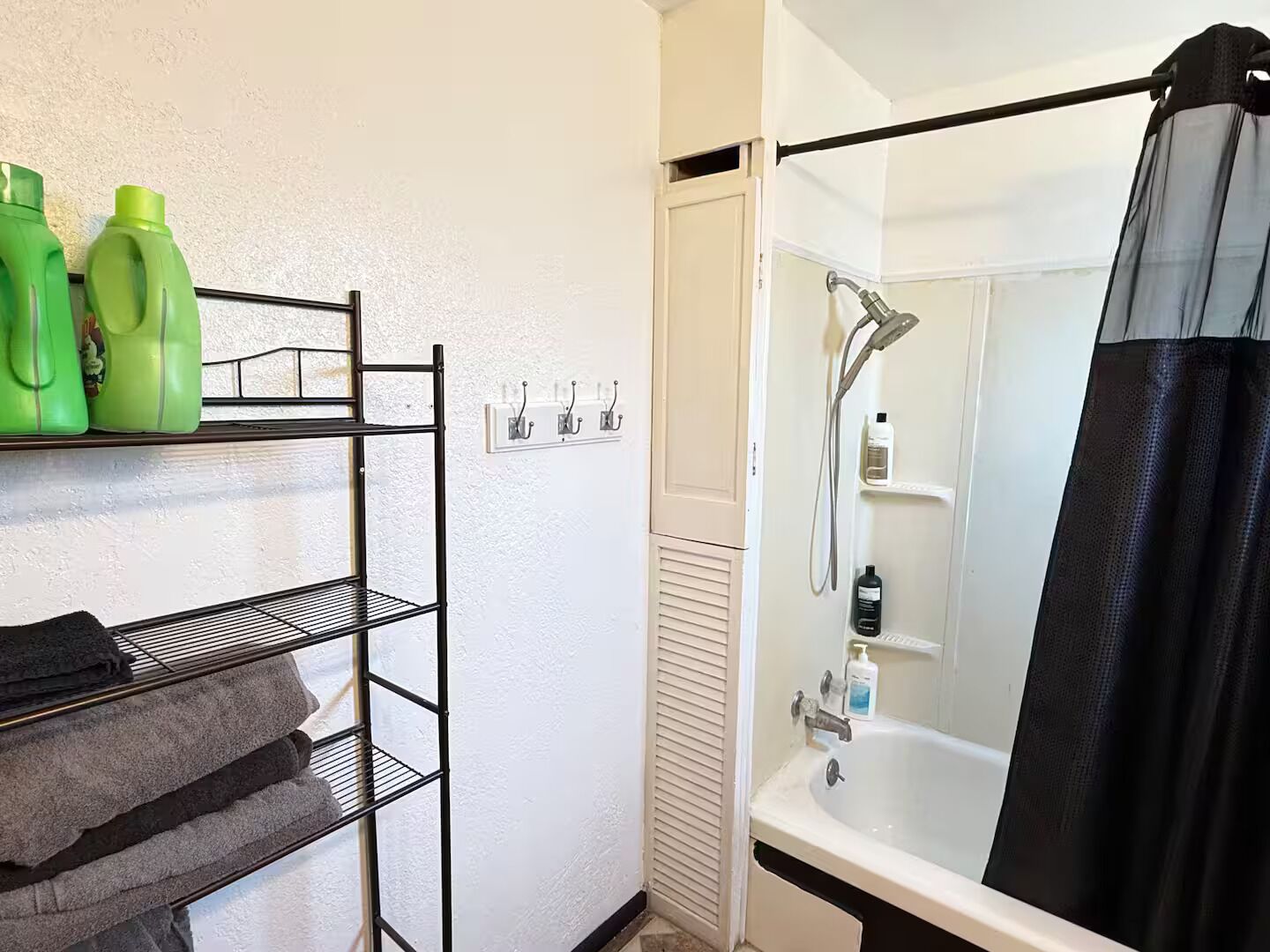 Et badeværelse med bruser, et håndklædestativ med håndklæder og en hylde med toiletartikler.