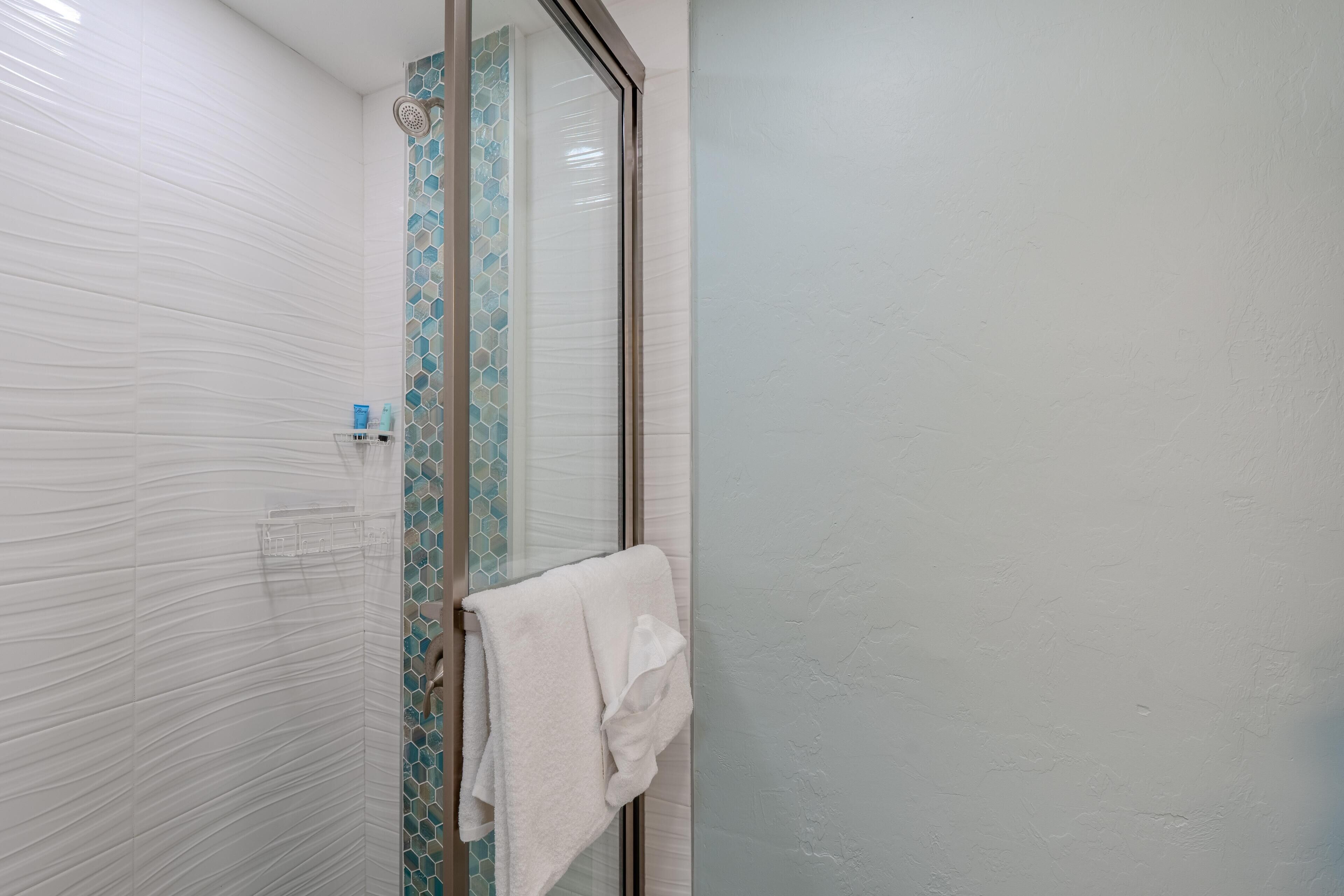 A bathroom with a glass shower door, a white towel hanging on the door, and a shelf with toiletries.