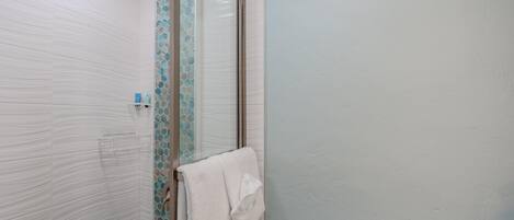 A bathroom with a glass shower door, a white towel hanging on the door, and a shelf with toiletries.