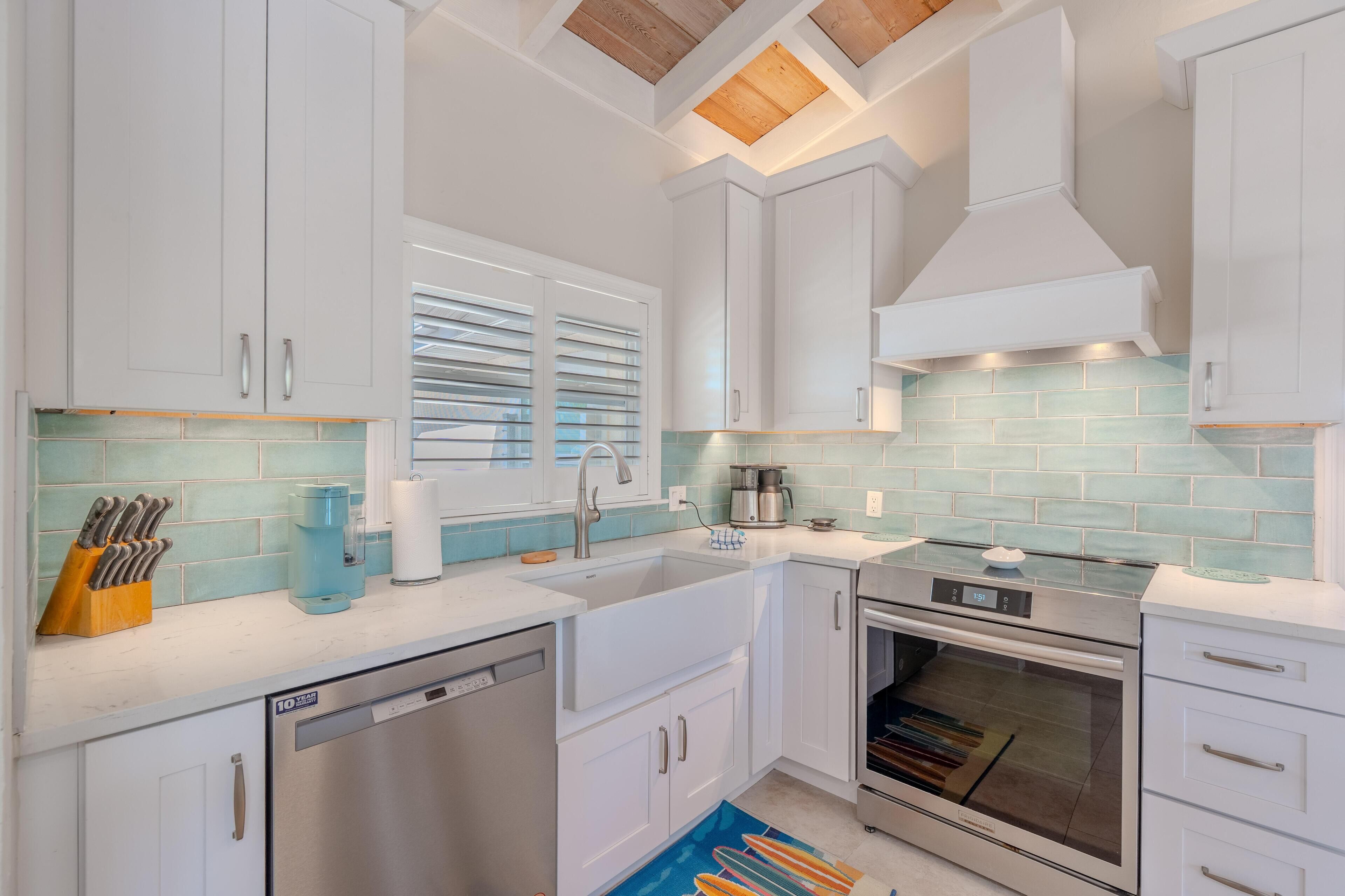 A modern kitchen with white cabinets, a stainless steel dishwasher, an oven, and a coffee maker.
