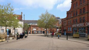 A public square with cobblestone pavement, a red brick building labeled 'BREWERS QU', and a sign for 'AVENUE'. - Brewmaster's Quarters (Weymouth)