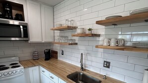 Een moderne keuken met witte kasten, houten werkbladen, een roestvrijstalen spoelbak en een inbouwmagnetron.