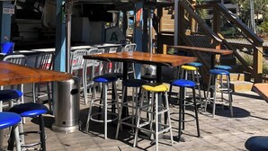 Een terras met tafels en krukken, een overdeeld gedeelte met een bord voor Bud Light, en een trap naar een parkeergarage.