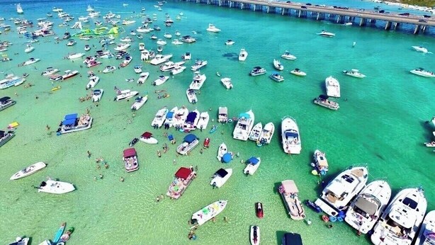 Een jachthaven met talloze boten afgemeerd en mensen op het strand.