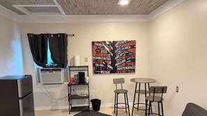 A compact living space with a kitchenette, a gray sofa, a round table with two chairs, and a large wall art piece. - Breakfast included/dartboard (Carlsbad)