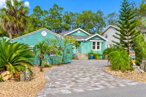 A two-story house with a green exterior, a front porch, and a driveway leading to the entrance. - Amazing Heated & Screen Pool w/ Stunning Design! (Crystal Beach)