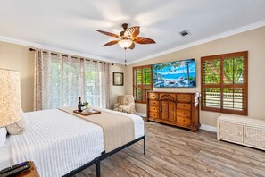 A bedroom with a bed, a wooden dresser, a ceiling fan, and a painting on the wall. - Amazing Heated & Screen Pool w/ Stunning Design! (Crystal Beach)