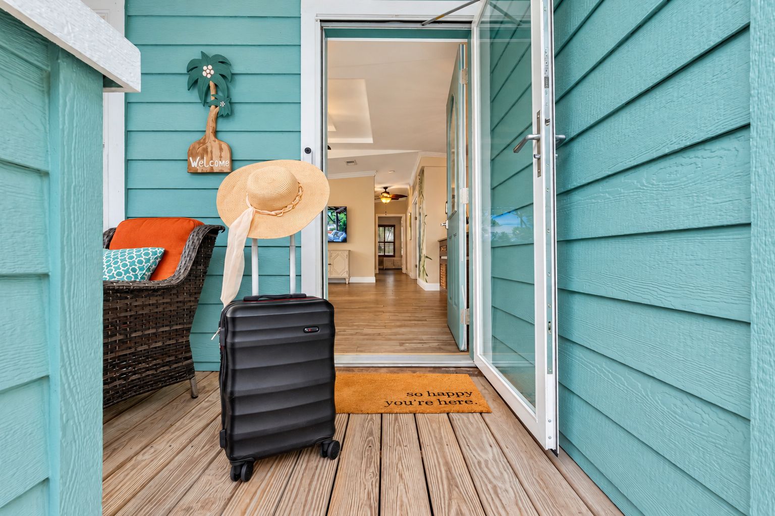 A wooden deck with a wicker chair, a suitcase, and a straw hat.