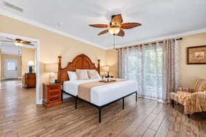A bedroom with a wooden bed, a ceiling fan, a nightstand, a chair, and a window with curtains. - Amazing Heated & Screen Pool w/ Stunning Design! (Crystal Beach)