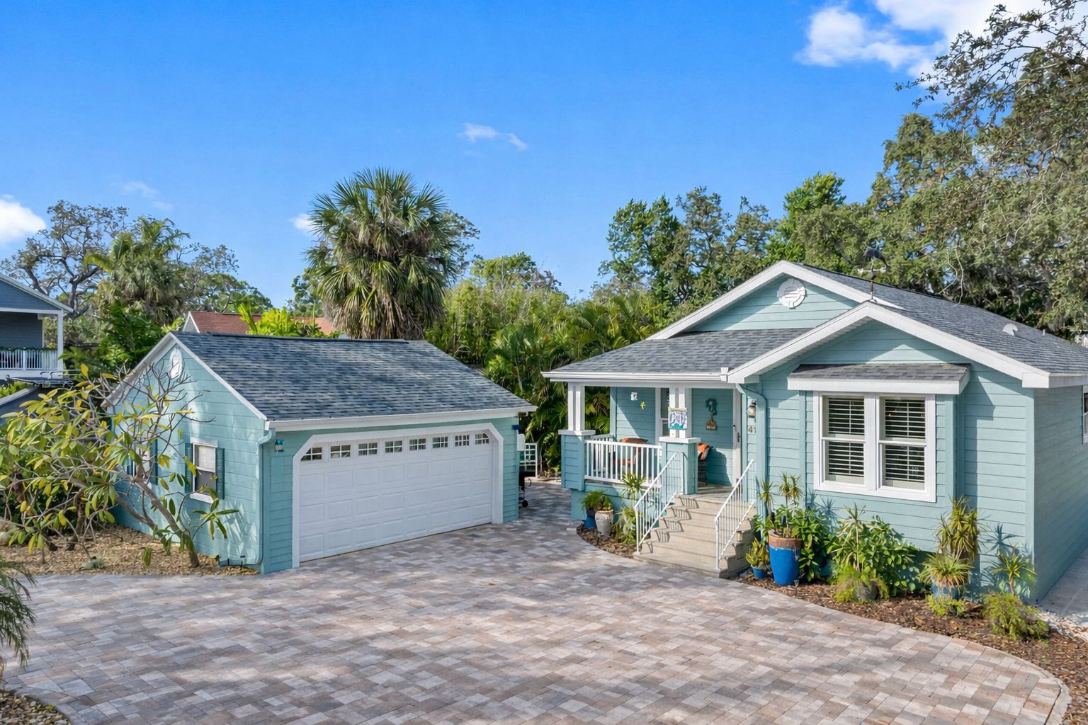 Une maison à deux étages avec un garage, une véranda et un petit jardin devant, agrémenté de plantes en pot.