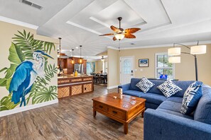 A spacious living room with a blue sofa, wooden coffee table, and a ceiling fan. - Amazing Heated & Screen Pool w/ Stunning Design! (Crystal Beach)