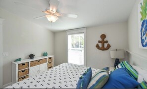 A bedroom with a bed, a ceiling fan, a window, a dresser with baskets, and a wall anchor decoration. - Coconut cottage Unit 1! (Holmes Beach)