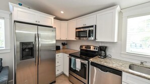 Una cocina con armarios blancos, electrodomésticos de acero inoxidable, microondas integrado, cafetera y lavavajillas.